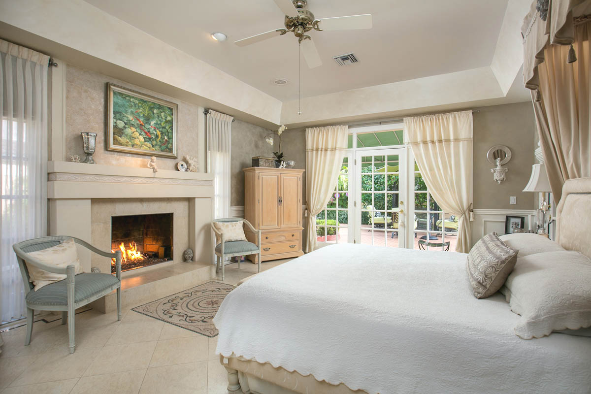 Master bedroom with fireplace with custom mantel & tray ceiling looking to the patio and pool area.                      